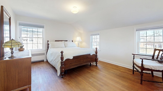 bedroom with baseboards, vaulted ceiling, radiator heating unit, and light wood finished floors