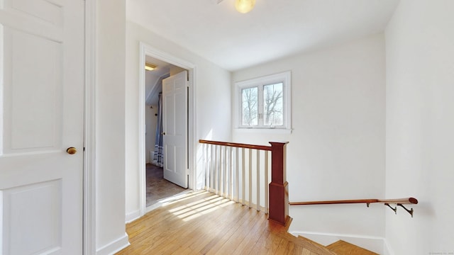 corridor with light wood-type flooring, an upstairs landing, and baseboards