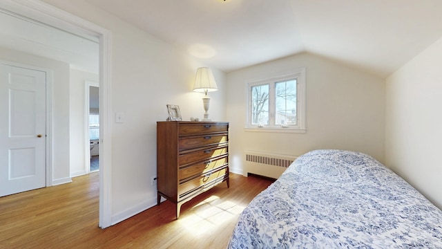 bedroom featuring baseboards, lofted ceiling, radiator, and light wood-style flooring