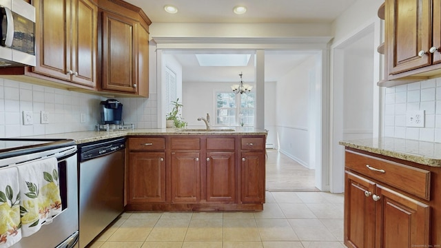 kitchen with a chandelier, light tile patterned floors, light stone counters, stainless steel appliances, and a sink