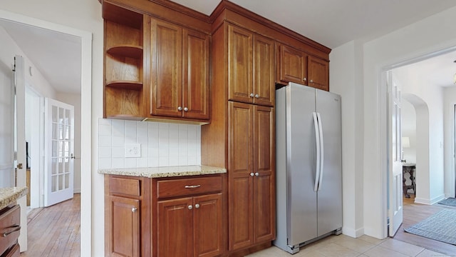 kitchen featuring open shelves, brown cabinetry, arched walkways, and freestanding refrigerator