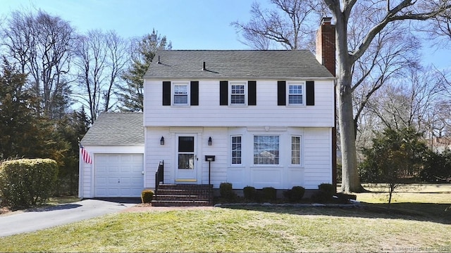 colonial inspired home with a shingled roof, a front yard, a chimney, driveway, and an attached garage