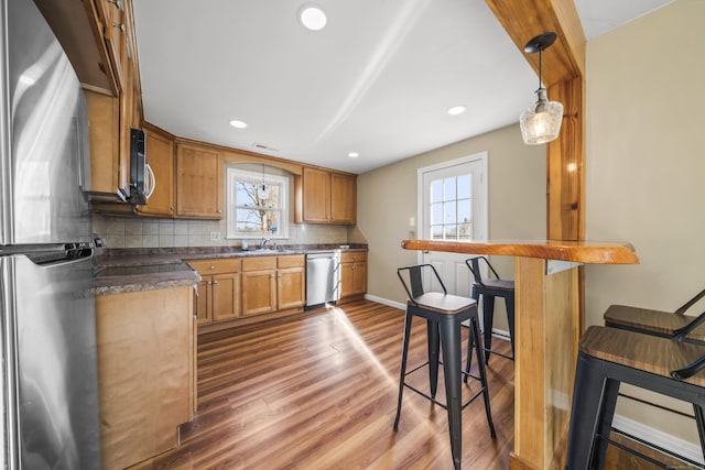 kitchen featuring a sink, backsplash, dark countertops, appliances with stainless steel finishes, and dark wood-style flooring