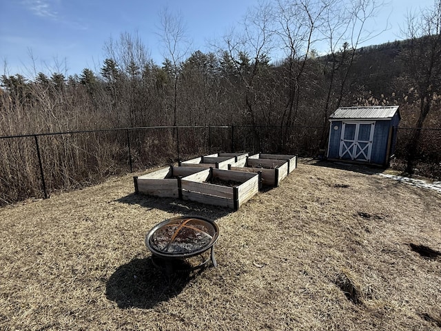 view of yard featuring a shed, fence, a forest view, a vegetable garden, and an outdoor structure