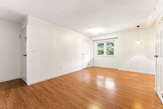 unfurnished room with light wood-type flooring, baseboards, and a textured ceiling