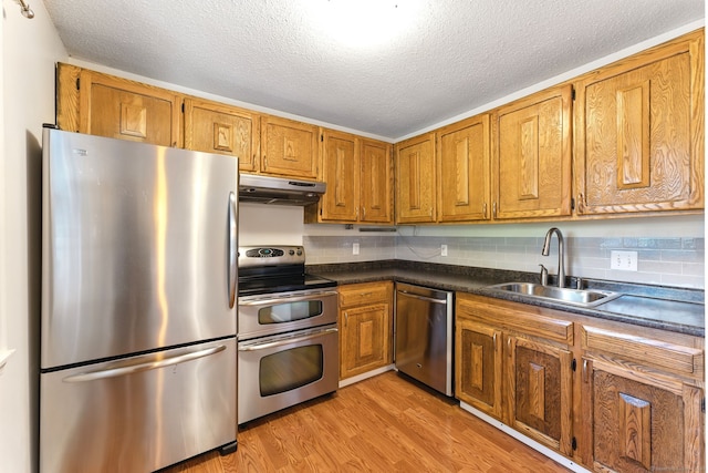 kitchen featuring brown cabinetry, a sink, stainless steel appliances, light wood-style floors, and under cabinet range hood