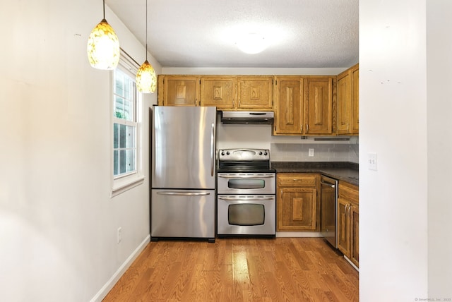 kitchen featuring dark countertops, backsplash, under cabinet range hood, light wood-type flooring, and appliances with stainless steel finishes