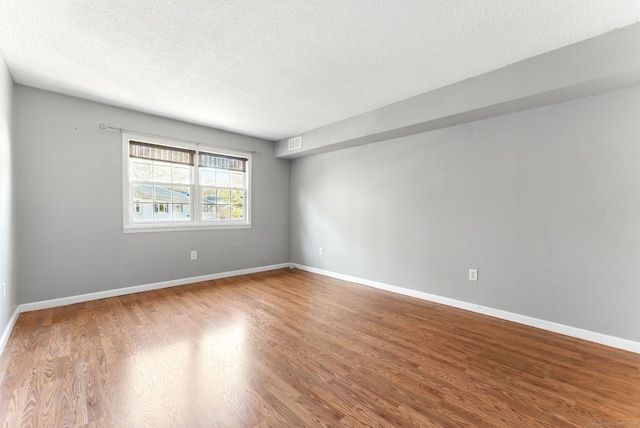 spare room featuring visible vents, baseboards, a textured ceiling, and wood finished floors