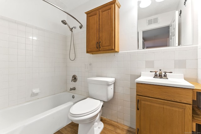 bathroom featuring tub / shower combination, toilet, vanity, wood finished floors, and tile walls