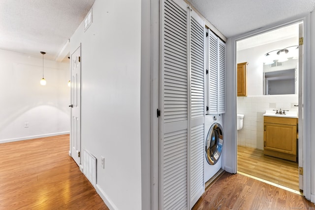 washroom featuring visible vents, washer / clothes dryer, a textured ceiling, tile walls, and light wood finished floors