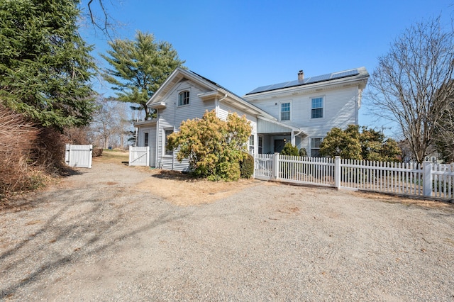 view of front of house with a fenced front yard, roof mounted solar panels, dirt driveway, and a gate