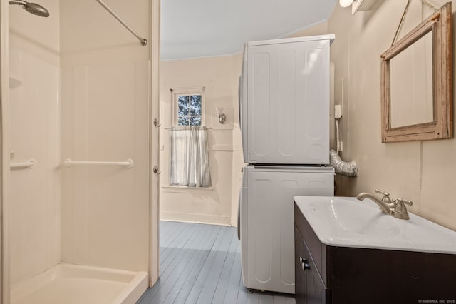 full bath featuring stacked washer and clothes dryer, vanity, a shower, and hardwood / wood-style flooring