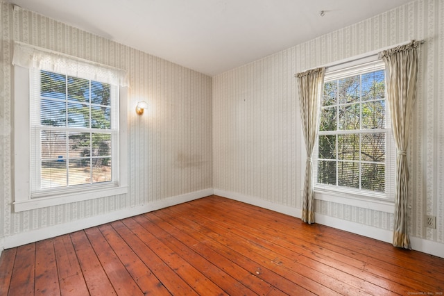 spare room featuring wood-type flooring, a healthy amount of sunlight, and wallpapered walls