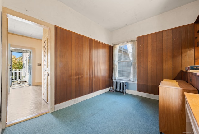 interior space featuring carpet flooring, wood walls, and radiator heating unit