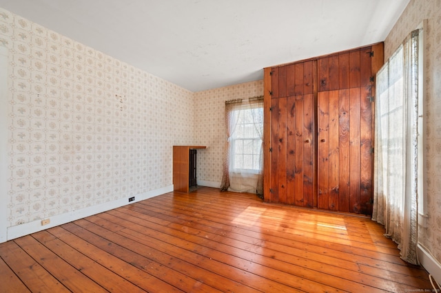 unfurnished room with light wood finished floors, wallpapered walls, and baseboards