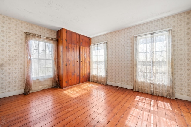 empty room featuring wallpapered walls, baseboards, and wood-type flooring