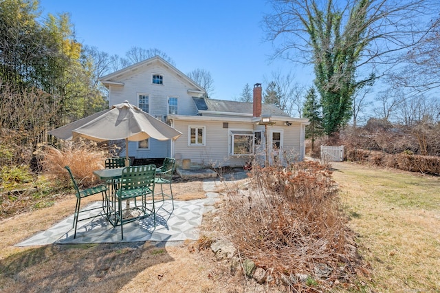 back of property with a lawn, a chimney, and a patio area