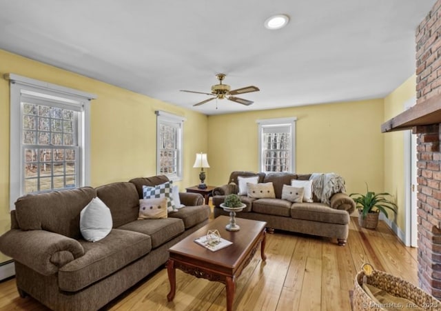 living area with light wood-type flooring, baseboard heating, a brick fireplace, and ceiling fan