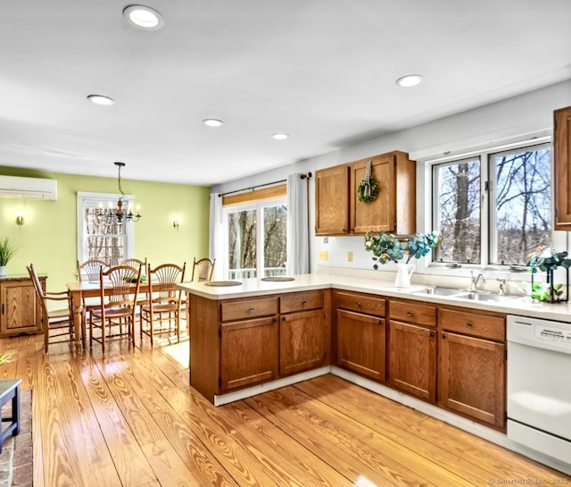 kitchen with light wood finished floors, a peninsula, white dishwasher, brown cabinetry, and a sink