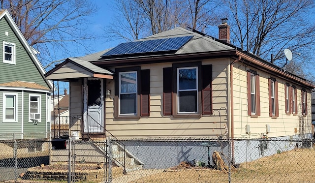 view of front of property featuring a shingled roof, a fenced front yard, roof mounted solar panels, a chimney, and a gate