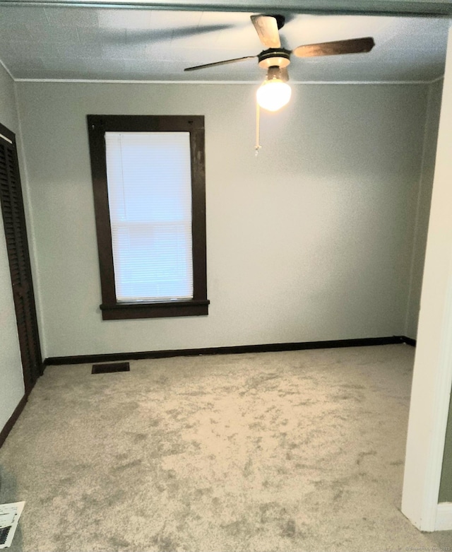 carpeted spare room with visible vents, ceiling fan, and baseboards