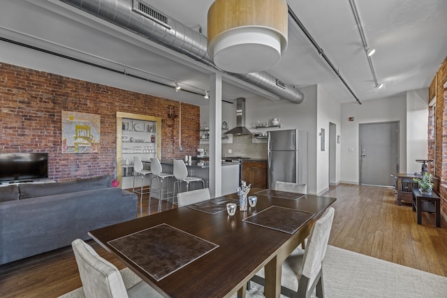 dining area with rail lighting, wood finished floors, visible vents, and brick wall