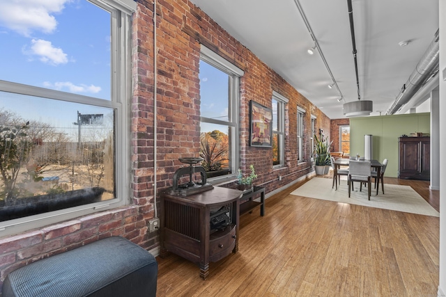 interior space with brick wall, rail lighting, and hardwood / wood-style flooring