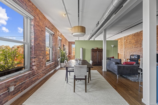 dining room featuring wood finished floors, brick wall, and rail lighting