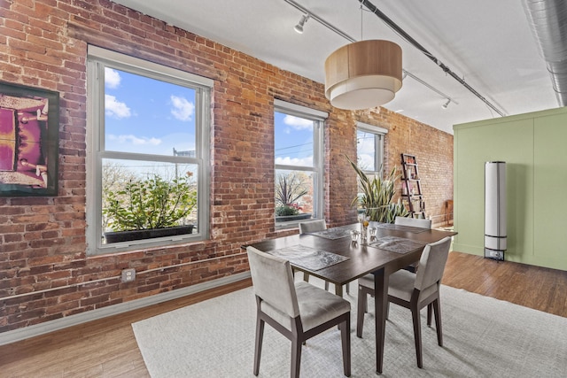 dining room featuring wood finished floors, brick wall, and rail lighting