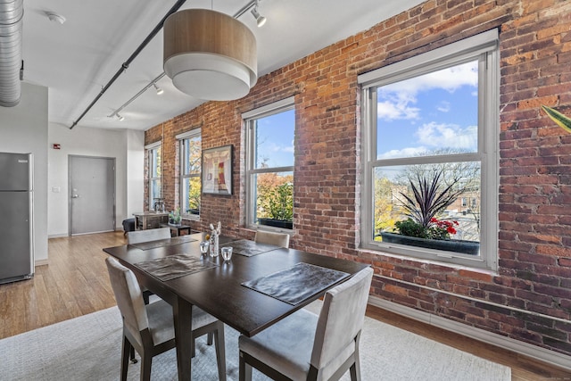 dining space with baseboards, brick wall, track lighting, and light wood finished floors