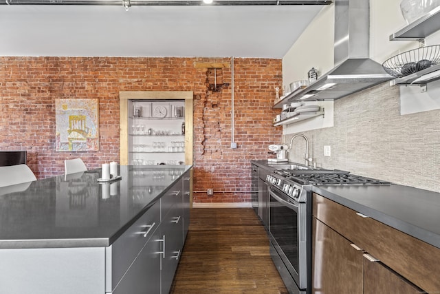 kitchen with dark countertops, wall chimney range hood, stainless steel gas range, and a sink