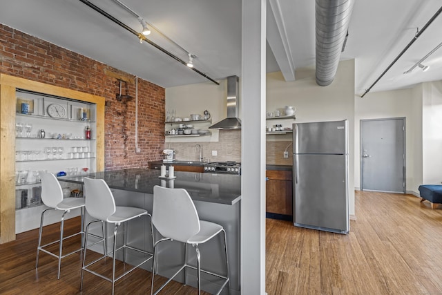 kitchen with wood finished floors, open shelves, freestanding refrigerator, dark countertops, and wall chimney exhaust hood