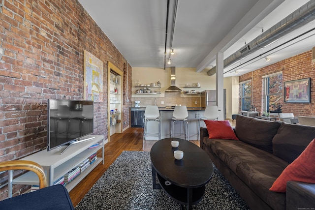 living room featuring dark wood-type flooring, brick wall, and track lighting