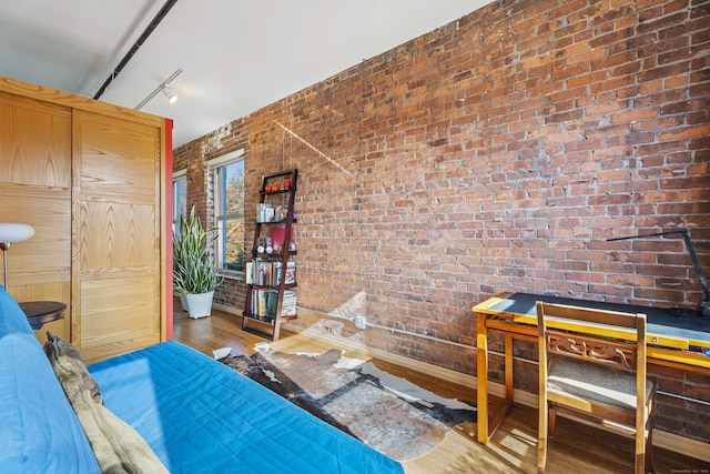 bedroom with track lighting, brick wall, baseboards, and wood finished floors