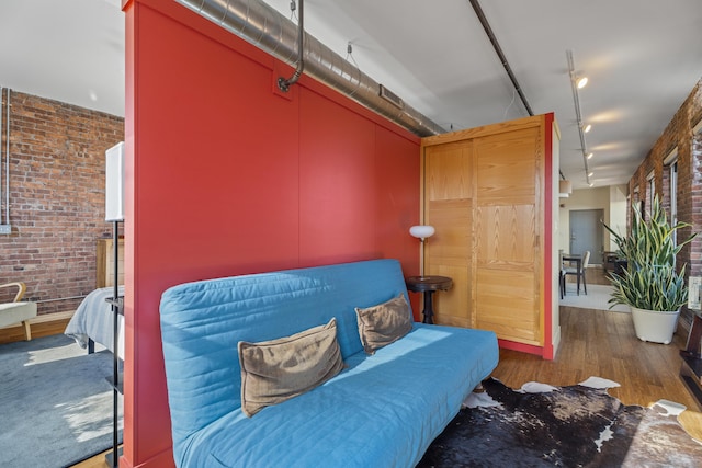 interior space featuring brick wall, rail lighting, and wood finished floors