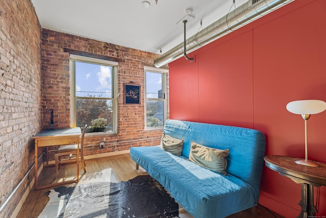 sitting room with brick wall and wood finished floors