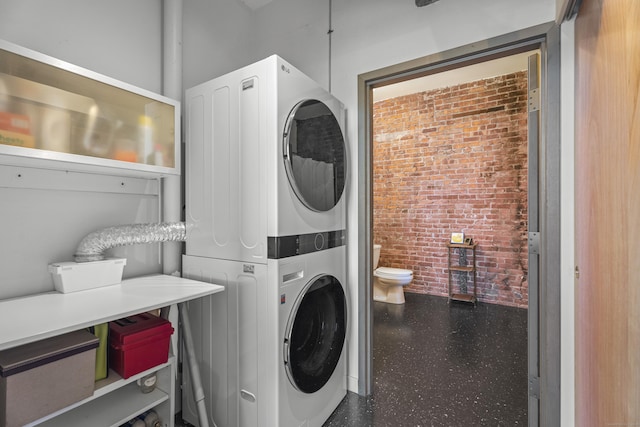 clothes washing area with brick wall, laundry area, and stacked washing maching and dryer