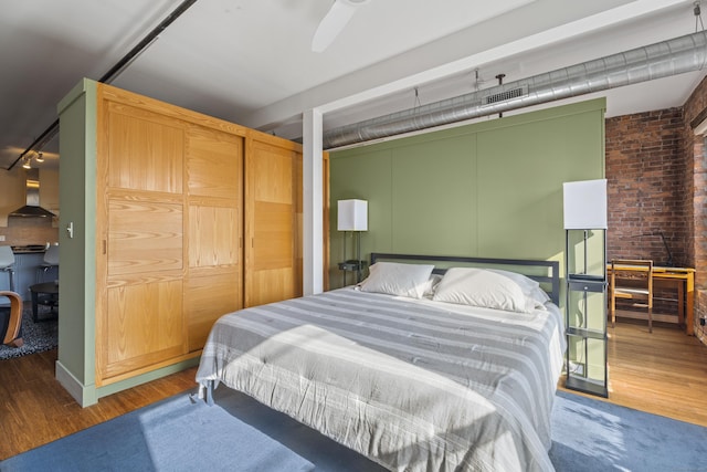 bedroom featuring visible vents, brick wall, track lighting, and wood finished floors