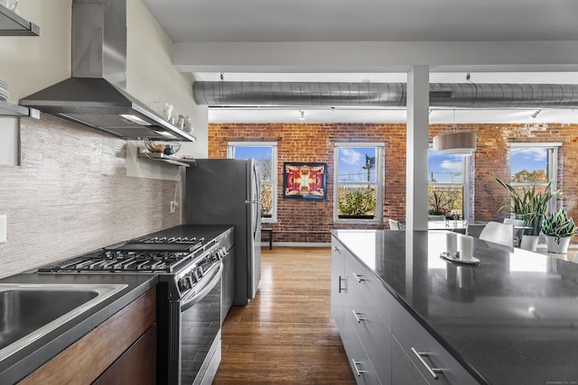 kitchen with stainless steel appliances, dark countertops, brick wall, and wall chimney range hood