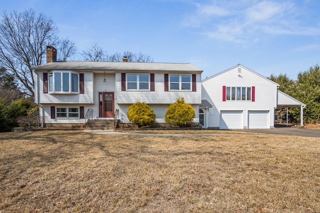 bi-level home with aphalt driveway, a garage, a chimney, and a front lawn