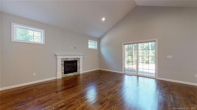 unfurnished living room featuring baseboards, high vaulted ceiling, a stone fireplace, and wood finished floors