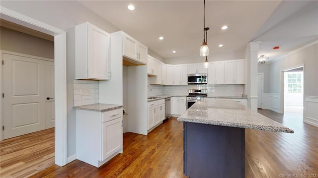 kitchen with light stone counters, appliances with stainless steel finishes, white cabinetry, and wood finished floors