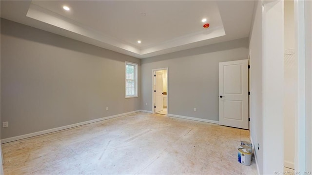 unfurnished bedroom with recessed lighting, a tray ceiling, baseboards, and ensuite bathroom