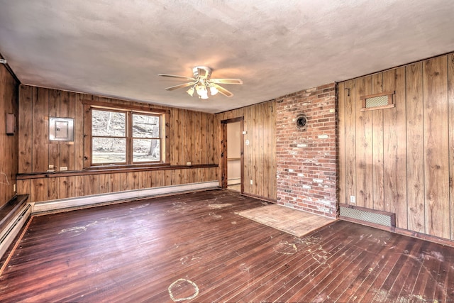 unfurnished room with ceiling fan, wood walls, wood-type flooring, and a baseboard radiator