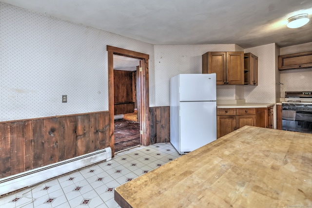 kitchen with a wainscoted wall, freestanding refrigerator, gas stove, wallpapered walls, and baseboard heating