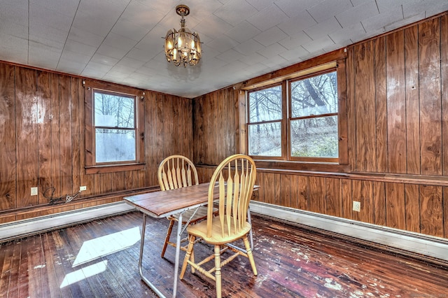 unfurnished dining area with a healthy amount of sunlight, a chandelier, wood walls, baseboard heating, and hardwood / wood-style flooring