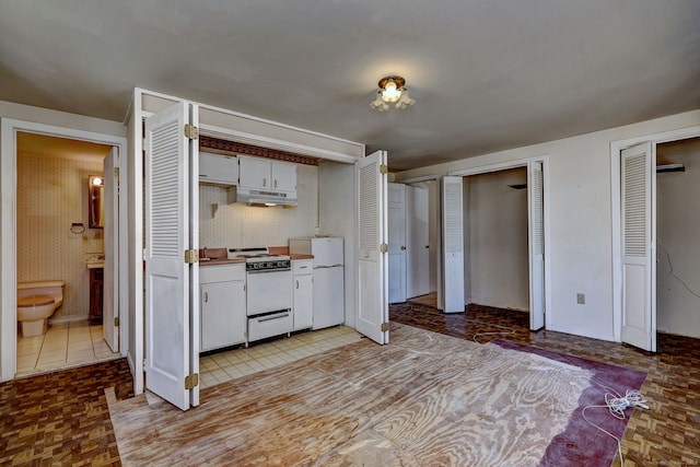 kitchen with under cabinet range hood, white appliances, and white cabinetry