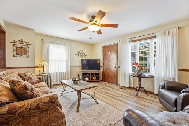 living room with visible vents, light wood-style flooring, plenty of natural light, and a ceiling fan