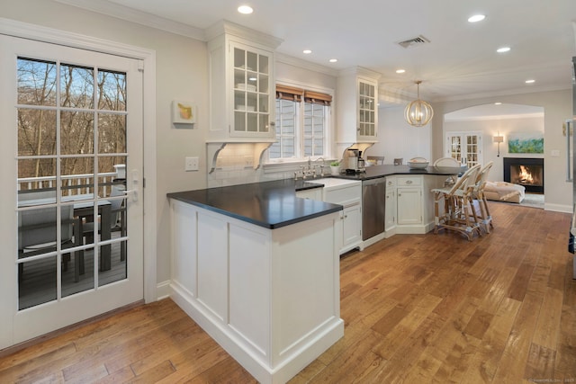 kitchen with dark countertops, visible vents, a warm lit fireplace, a peninsula, and stainless steel dishwasher