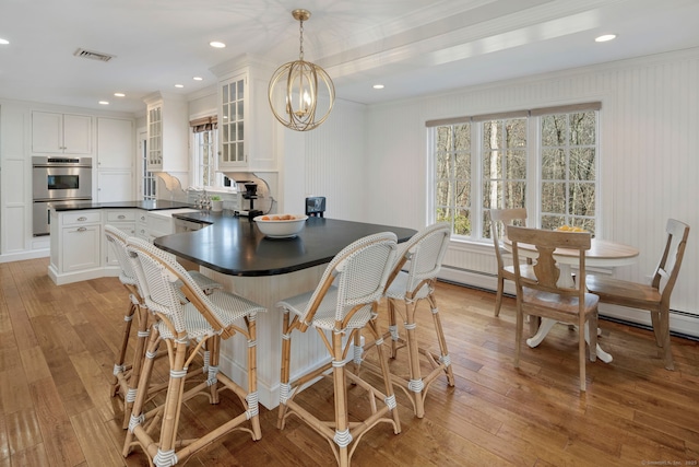 dining space with an inviting chandelier, visible vents, light wood finished floors, and a baseboard radiator